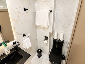 Ein modernes Badezimmer mit Marmorverkleidung, einer schwarzen Toilette, einem Waschbecken mit Seifenspender und einem Handtuchhalter.
