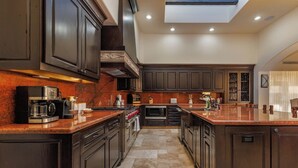 A modern kitchen with dark cabinetry, a central island, and a skylight. - Luxury 4BR Villa | Pool, Jacuzzi & Golf Views (Cabo San Lucas)