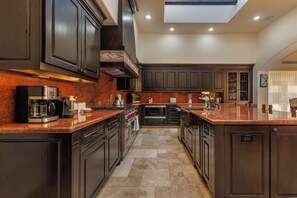A modern kitchen with dark cabinetry, a central island, and a skylight. - Luxury 4BR Villa | Pool, Jacuzzi & Golf Views (Cabo San Lucas)