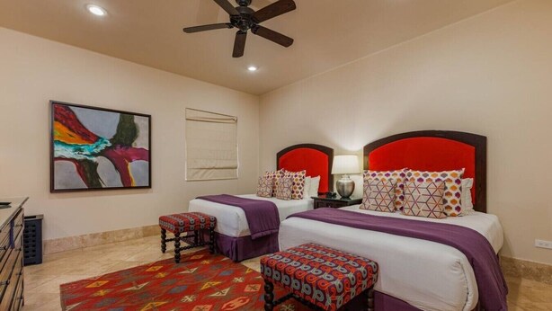 A hotel room with two beds, a ceiling fan, a colorful abstract painting, and a patterned rug. - Luxury 4BR Villa | Pool, Jacuzzi & Golf Views (Cabo San Lucas)