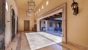 A spacious hallway with a tiled floor, a bench, and a view into a covered outdoor area with seating. - Luxury 4BR Villa | Pool, Jacuzzi & Golf Views (Cabo San Lucas)