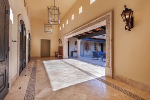 A spacious hallway with a tiled floor, a bench, and a view into a covered outdoor area with seating. - Luxury 4BR Villa | Pool, Jacuzzi & Golf Views (Cabo San Lucas)