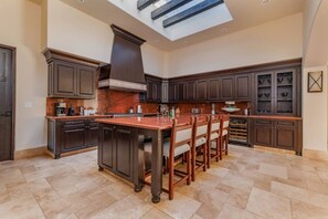 A spacious kitchen with dark wood cabinetry, a central island with bar stools, and a skylight above. - Luxury 4BR Villa | Pool, Jacuzzi & Golf Views (Cabo San Lucas)