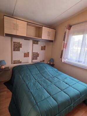 Une chambre à coucher avec un lit, des armoires en bois, une étagère fixée au mur et une fenêtre avec des rideaux.