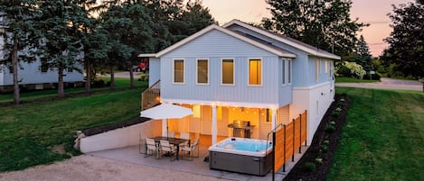 A two-story house with a patio area, outdoor seating, and a hot tub.