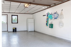 A room with a tiled floor, a white refrigerator, a window with a view, and a wall with hanging items.