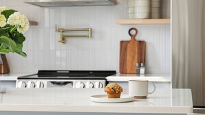 Une cuisine dotée d’un îlot central, de meubles blancs et d’une hotte de cuisinière en acier inoxydable.