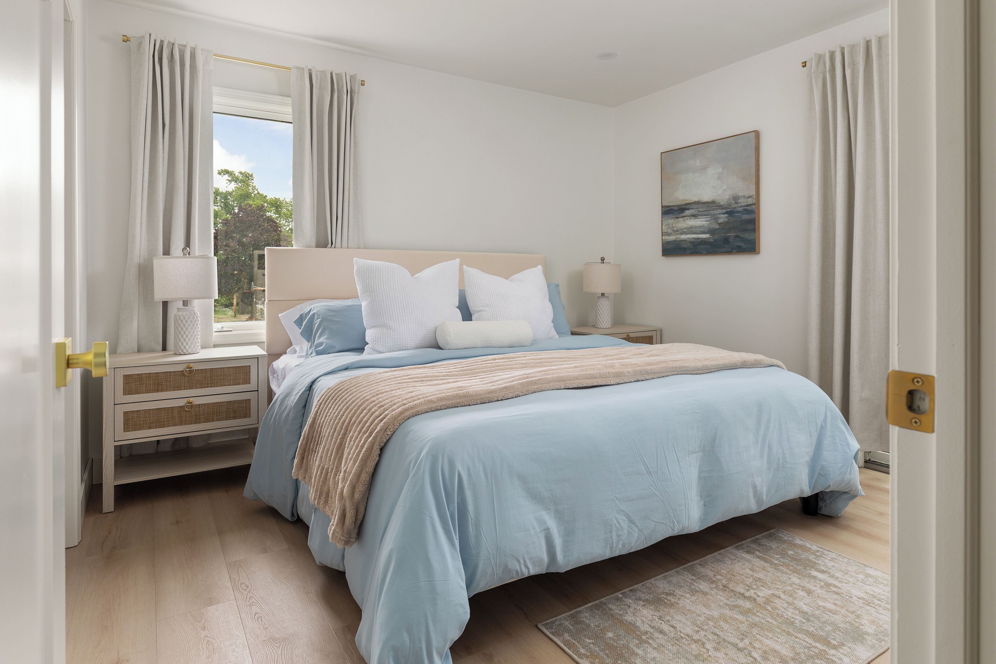 A bedroom with a bed, nightstand, lamp, and a painting on the wall.