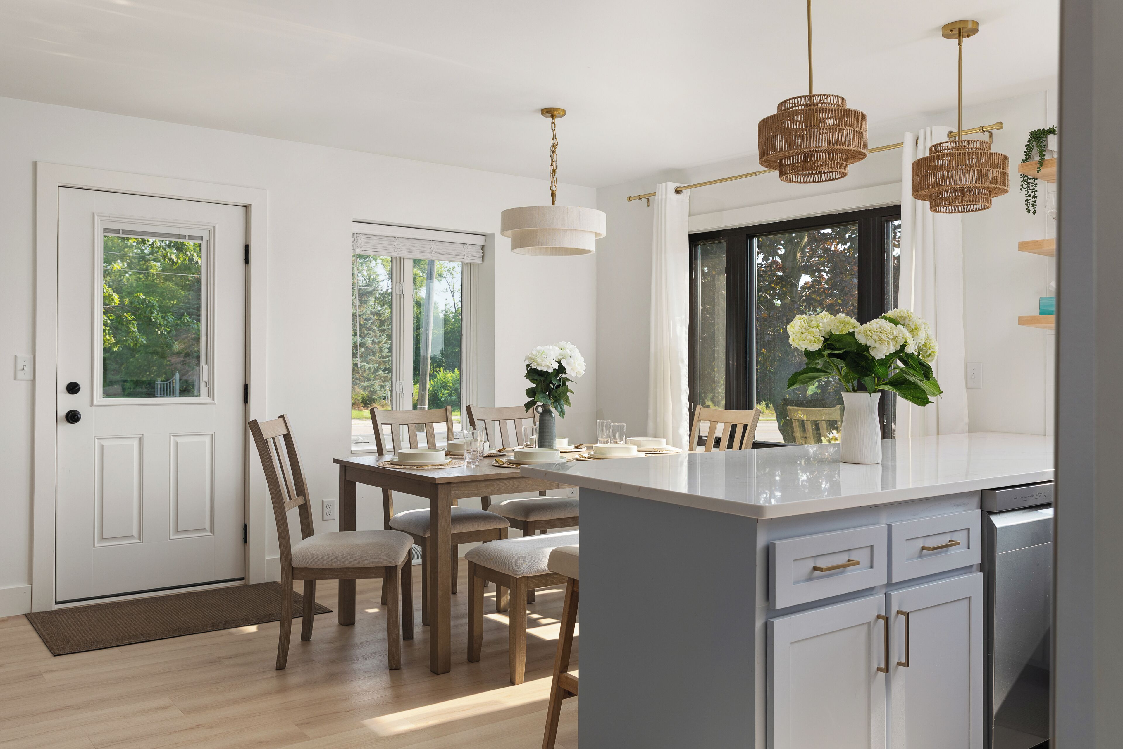 A modern kitchen with a central island, wooden chairs, a dining table, and pendant lighting.