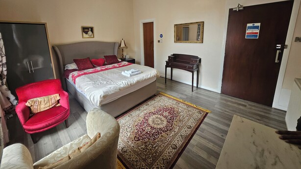 Een hotelkamer met een bed, een bureau, een stoel, een kledingkast, een spiegel en een kroonluchter.