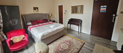 A hotel room with a bed, a desk, a chair, a wardrobe, a mirror, and a chandelier.