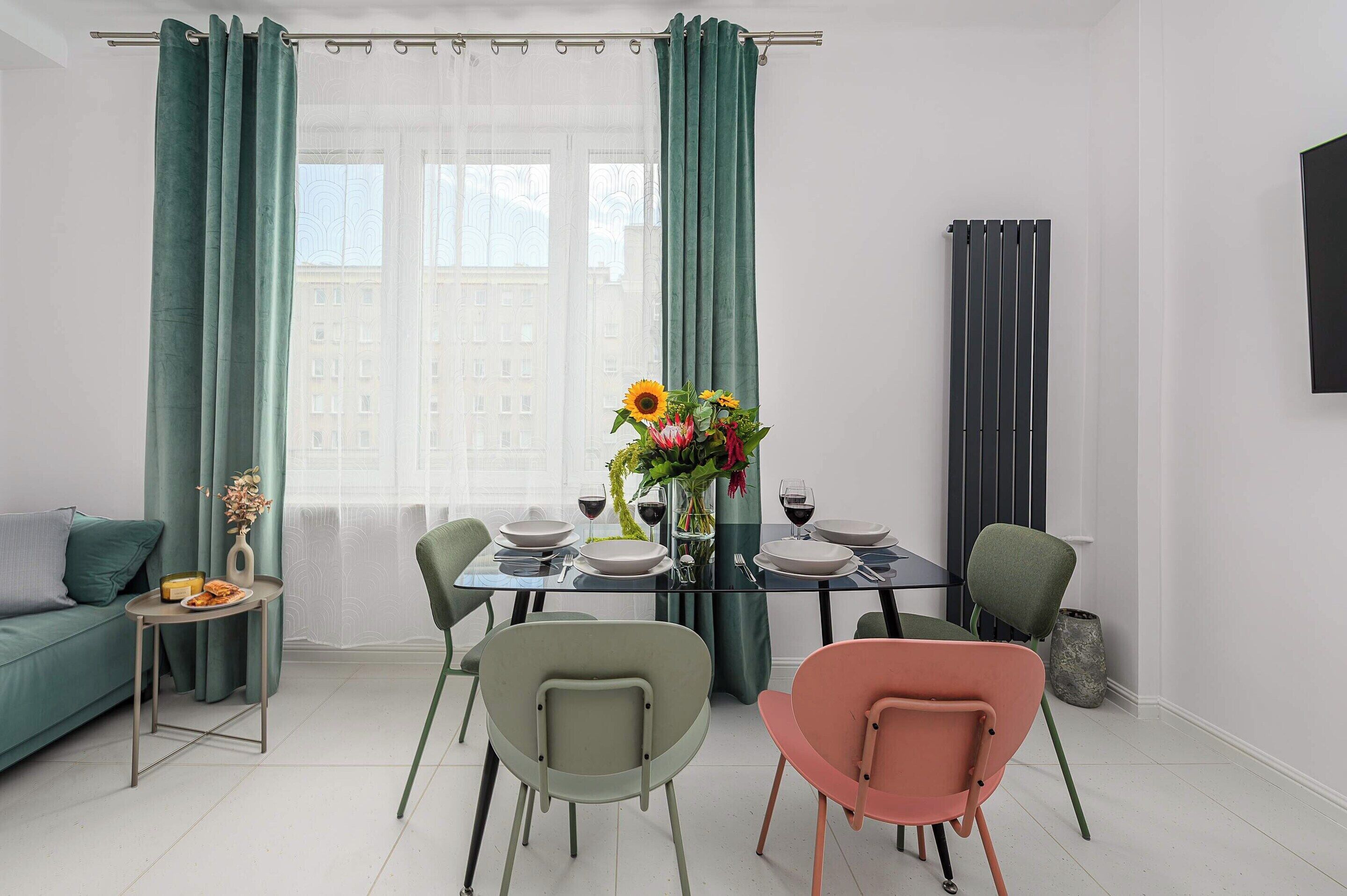 A dining area with a table set for two, two chairs, a sofa, and a small side table with a vase and a plate of food.
