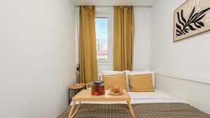 A hotel room with a bed, a bedside table with a kettle and pastries, and a window with curtains. - Magnificent Beach House for 6 (Warsaw)