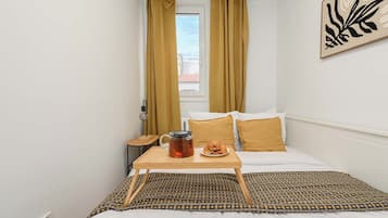 Ein Hotelzimmer mit Bett, Nachttisch mit Wasserkocher und Gebäck, sowie einem Fenster mit Vorhängen.
