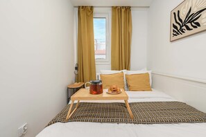 Ein Hotelzimmer mit Bett, Nachttisch mit Wasserkocher und Gebäck, sowie einem Fenster mit Vorhängen.
