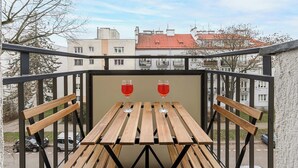 A balcony with a wooden table and two wine glasses, overlooking a residential area with buildings and parked cars. - Magnificent Beach House for 6 (Warsaw)