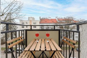Ein Balkon mit einem Holztisch und zwei Weingläsern, mit Blick auf ein Wohngebiet mit Gebäuden und parkenden Autos.