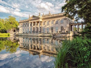 Ein klassizistisches Gebäude mit einer symmetrischen Fassade, großen Fenstern und Spiegelung im Wasser.