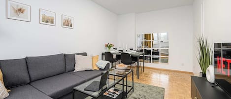 A modern living room with a grey sofa, a glass coffee table, and a dining area with a white table and chairs.