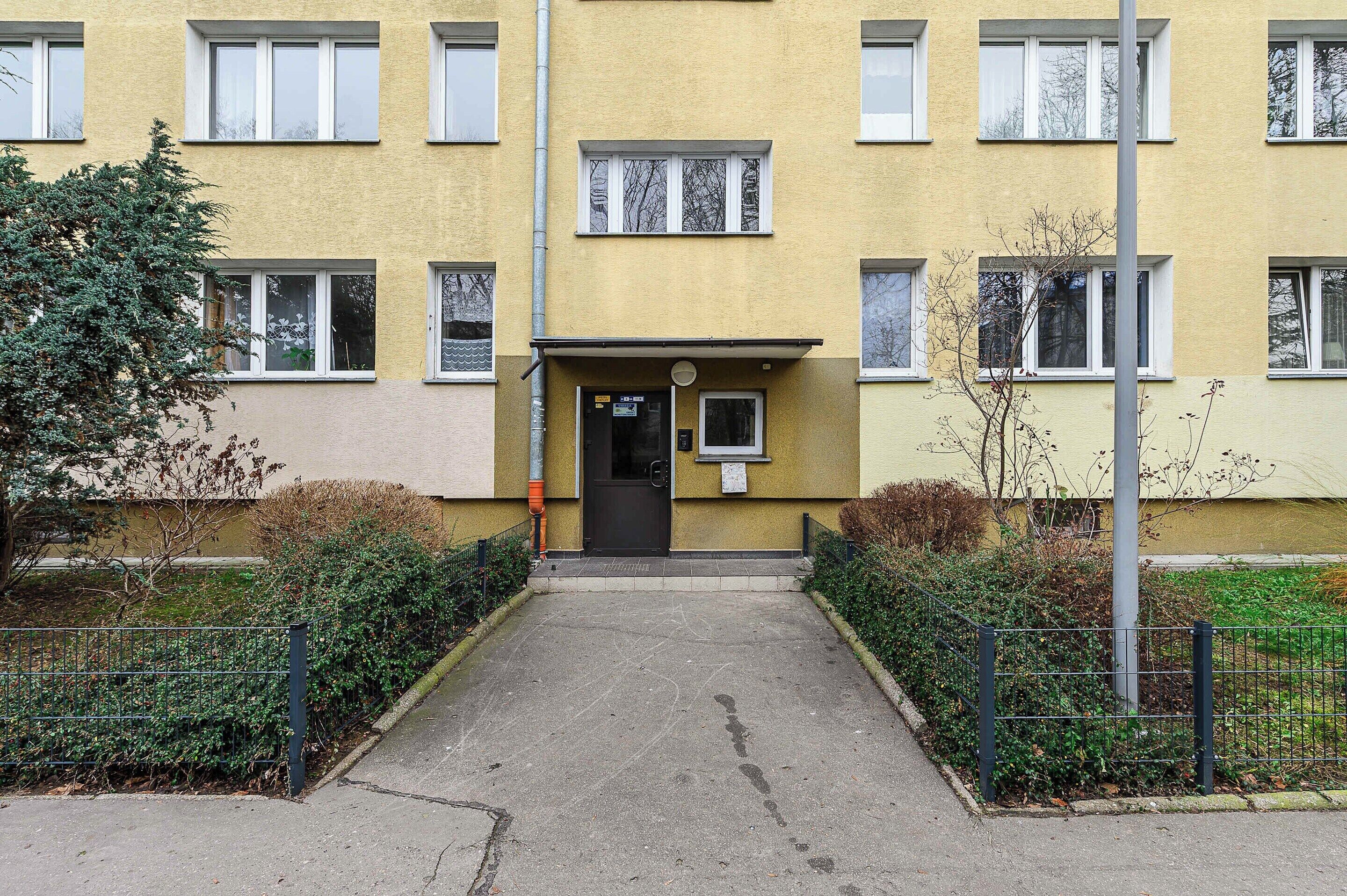 A yellow building with a central entrance, multiple windows, and a small sign above the door.