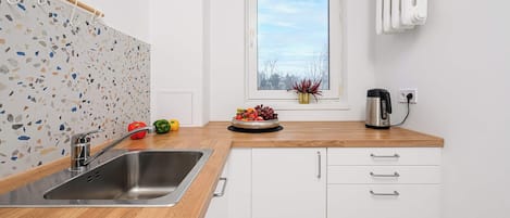 A modern kitchen with a stainless steel sink, wooden countertop, white cabinets, and a window with a view of the sky.
