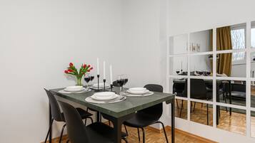 Un coin repas avec une table dressée pour quatre personnes, des chaises, un vase rempli de fleurs rouges et une fenêtre donnant sur un beau paysage.