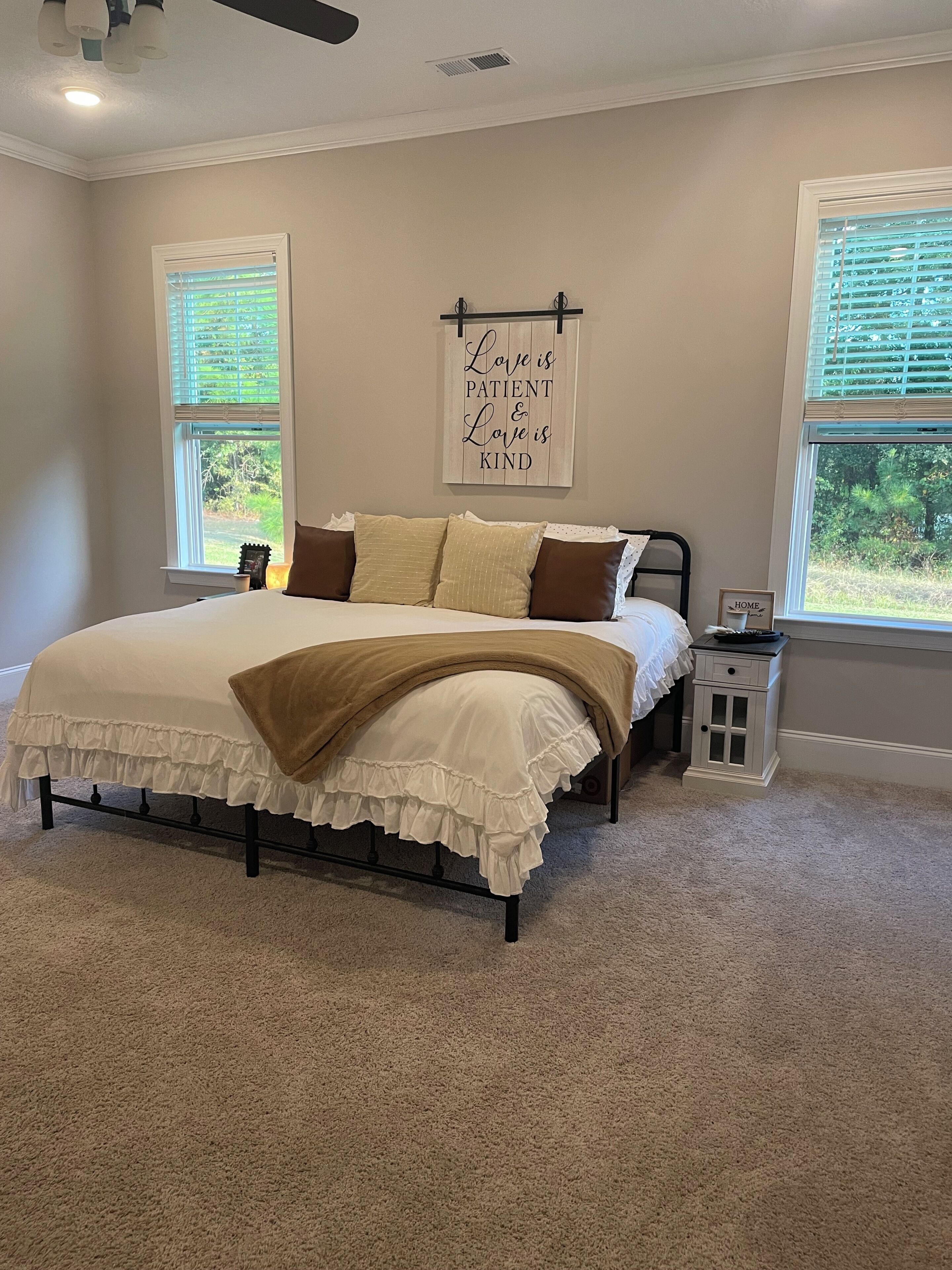 A bedroom with a bed, two windows, a bedside table, and a wall with a motivational quote.