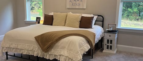 Ein Schlafzimmer mit einem Bett, zwei Fenstern, einem Nachttisch und einer Wand mit einem motivierenden Zitat.