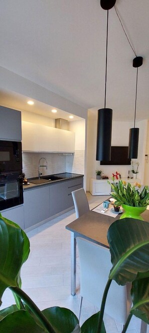 A modern kitchen with a built-in oven, a dining area with a table and chairs, and a hanging pendant light.