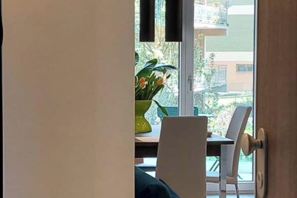 A room with a dining table, chairs, a potted plant, and a view of the outside.