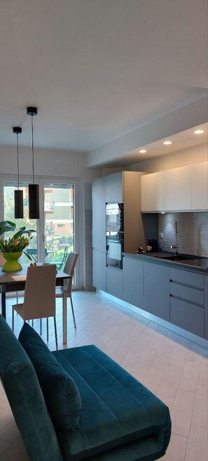 A modern kitchen with grey cabinets, a stainless steel refrigerator, and a dining area with a green sofa and chairs. - Interior of Apartment 5 (Lanciano)