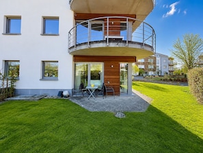 A modern residential building with a balcony, a patio with outdoor furniture, and a well-maintained lawn.