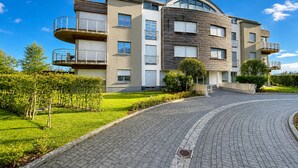 Un edificio residencial de varios pisos con balcones, un techo curvo y un camino de entrada pavimentado.