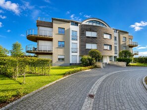 Un edificio residencial de varios pisos con balcones, un techo curvo y un camino de entrada pavimentado.