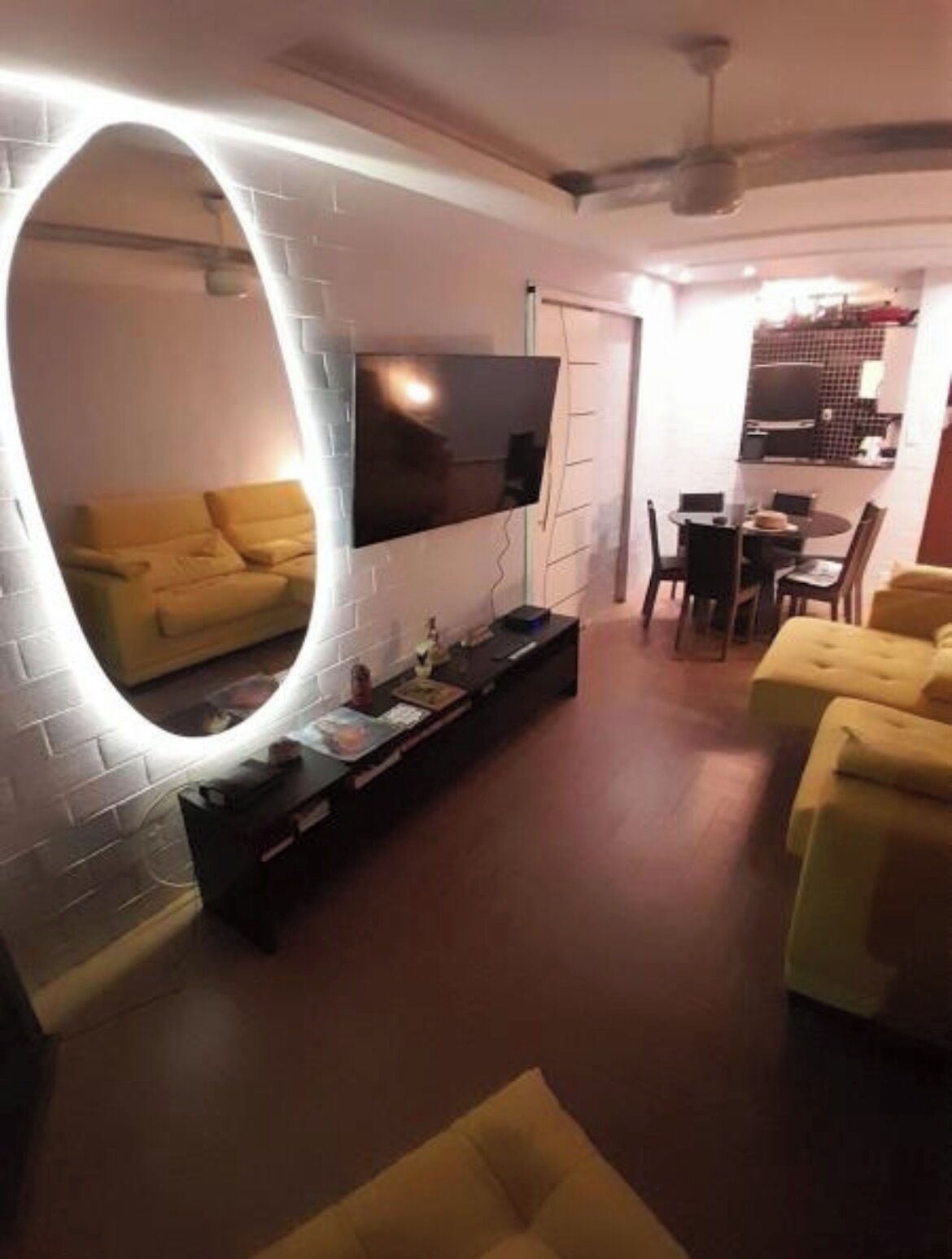 Ein Wohnzimmer mit einem Flachbildfernseher an einer weißen Ziegelwand, einer Couch, einem Couchtisch und einem Essbereich mit Tisch und Stühlen.