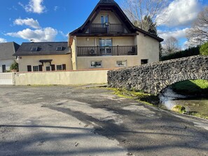 A two-story building with a stone bridge over a water channel, a gravel driveway, and a white fence. - Spacious House in the Heart of Béarn for 7 People (Ogeu-les-Bains)