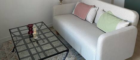 A living room with a sofa, a glass coffee table, and a patterned rug.