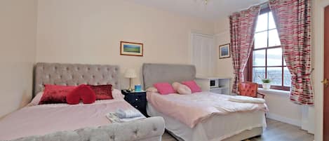Quarto com duas camas, um candelabro, uma janela com cortinas e um tapete.