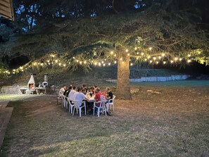 An outdoor dining area with stone tables and chairs, surrounded by a stone wall and a tree with string lights. - Spacious Villa with Private Park in Verucchio (Emilia-Romagna)