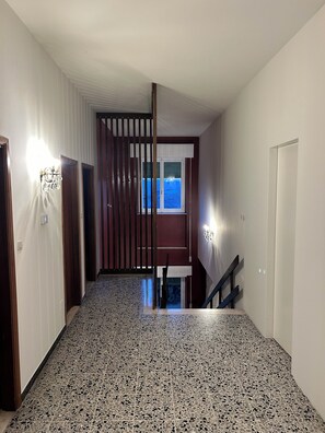 A hallway with a terrazzo floor, a wooden door, a window with blinds, and a wall-mounted light fixture. - Spacious Villa with Private Park in Verucchio (Emilia-Romagna)