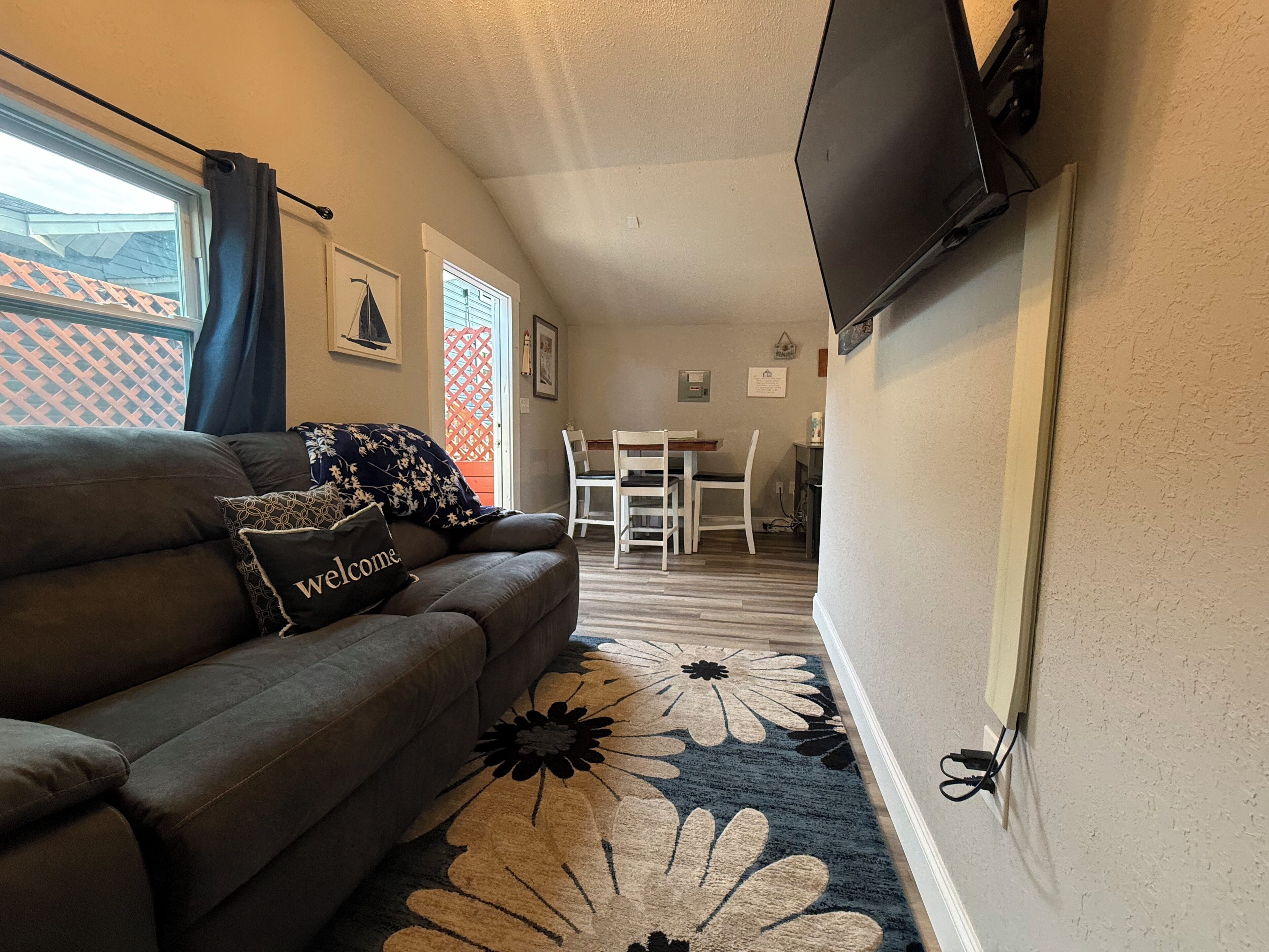A living room with a sofa, a television mounted on the wall, and a dining area with chairs and a table.
