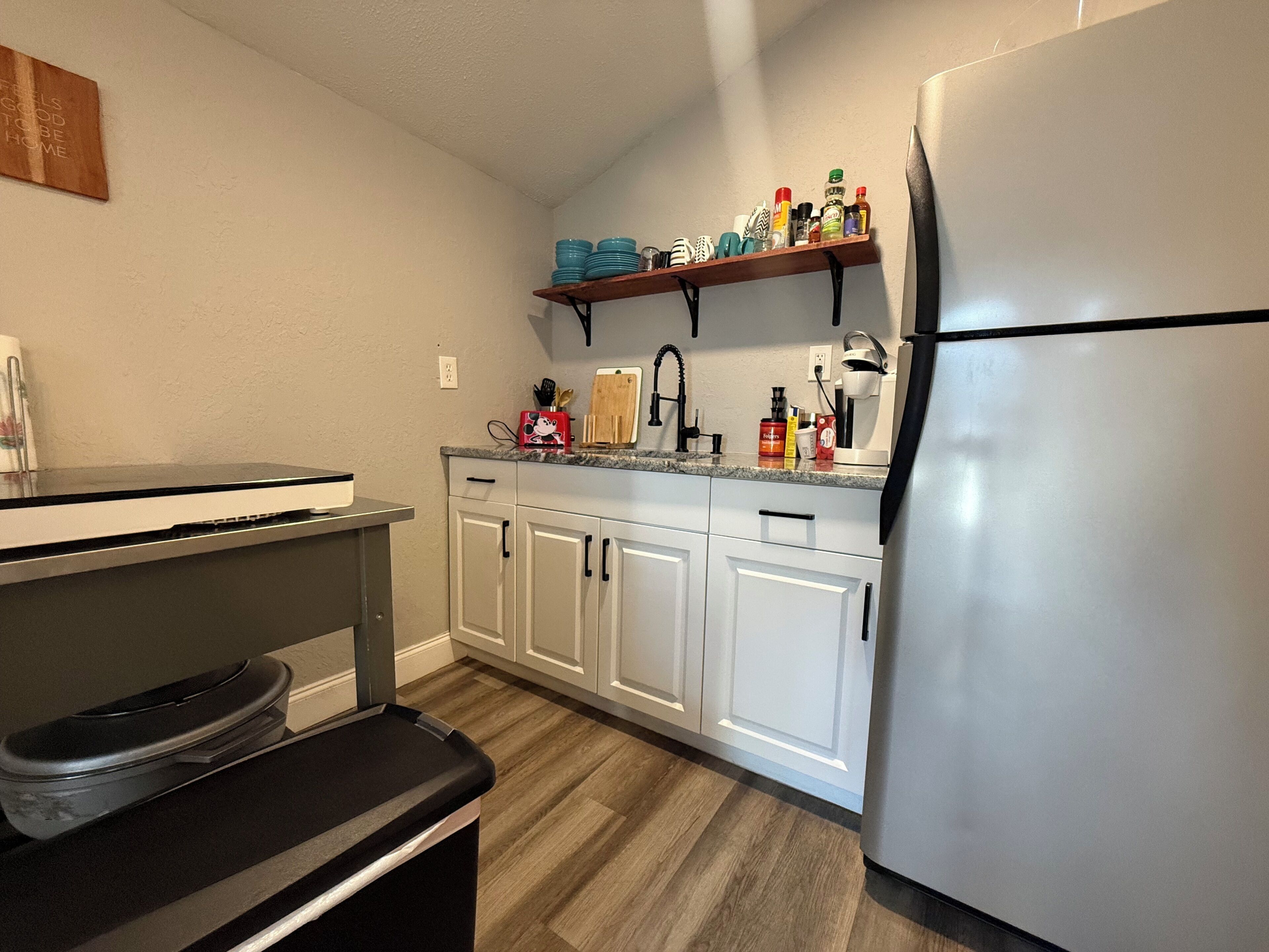 A kitchen with white cabinets, a stainless steel refrigerator, and a countertop with various items.