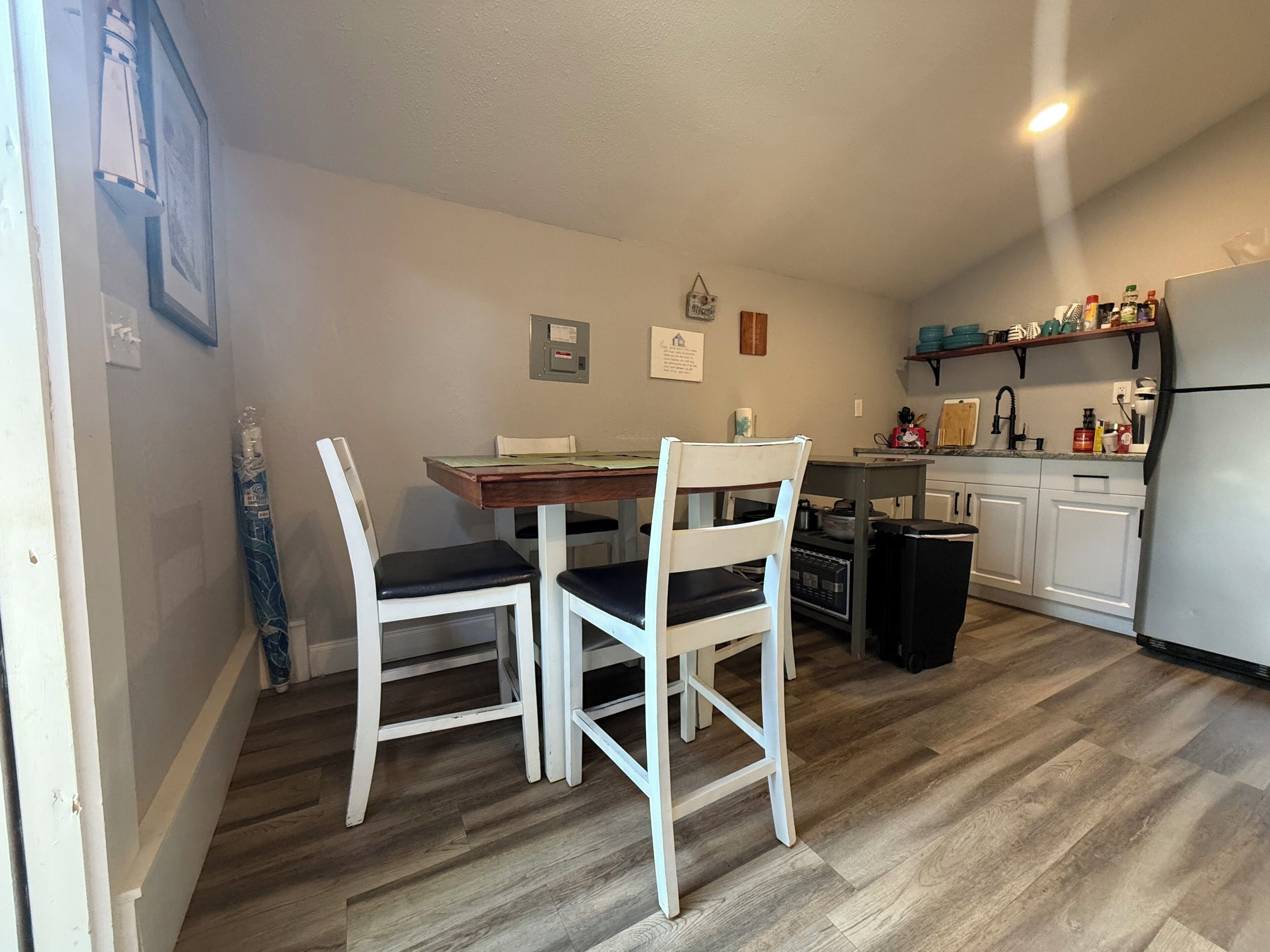 Une cuisine de taille réduite avec des meubles blancs, une table à manger en bois et deux chaises blanches.