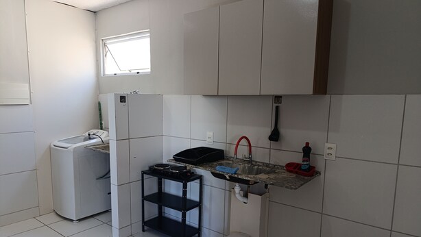 A compact kitchen with a washing machine, a sink with a red faucet, and a small stool.