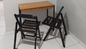 A corner room with a wooden table and two black chairs, a hexagonal wall decoration, and a white tiled floor.