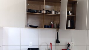 A kitchen with a sink, stove, cabinets, and a trash bin.