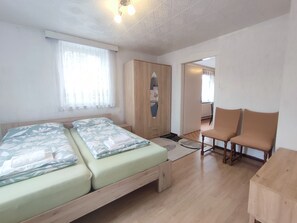A bedroom with two beds, a wardrobe, a desk, and a chair.