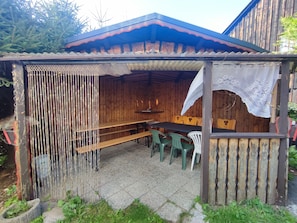 A covered outdoor seating area with a wooden table and chairs, a decorative fence, and a tiled floor.