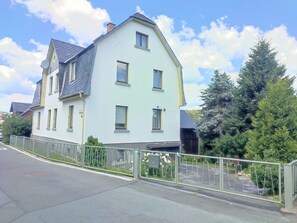 A two-story residential building with a light facade, multiple windows, and a gated driveway.