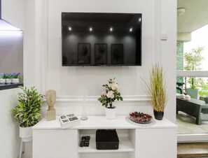 A modern living room with a flat-screen TV mounted on the wall, a white console table with decorative items, and a view of the outdoors through a window. - Spacious Central Warsaw Apartment (Warsaw)